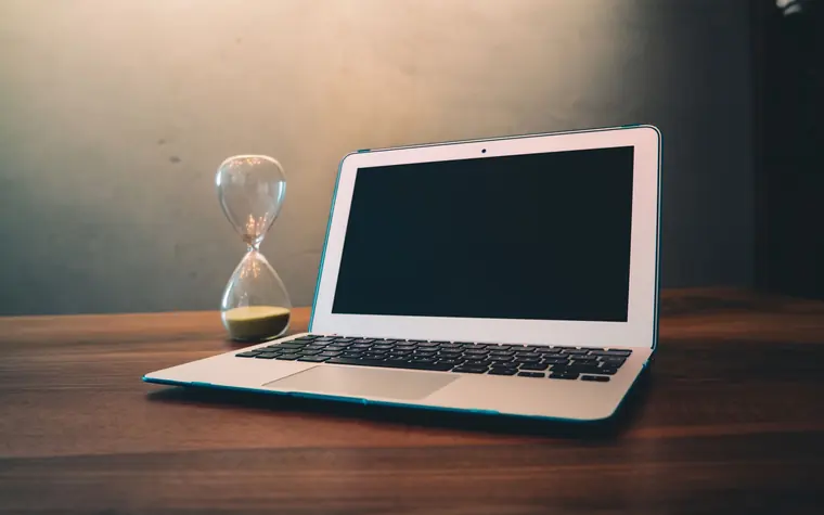 Hourglass sitting beside an open laptop.