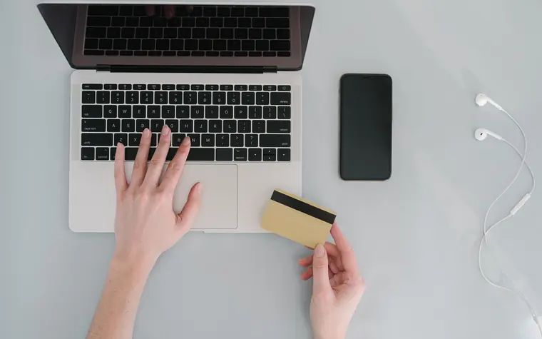 Person holding a bank card at a laptop during an online checkout.