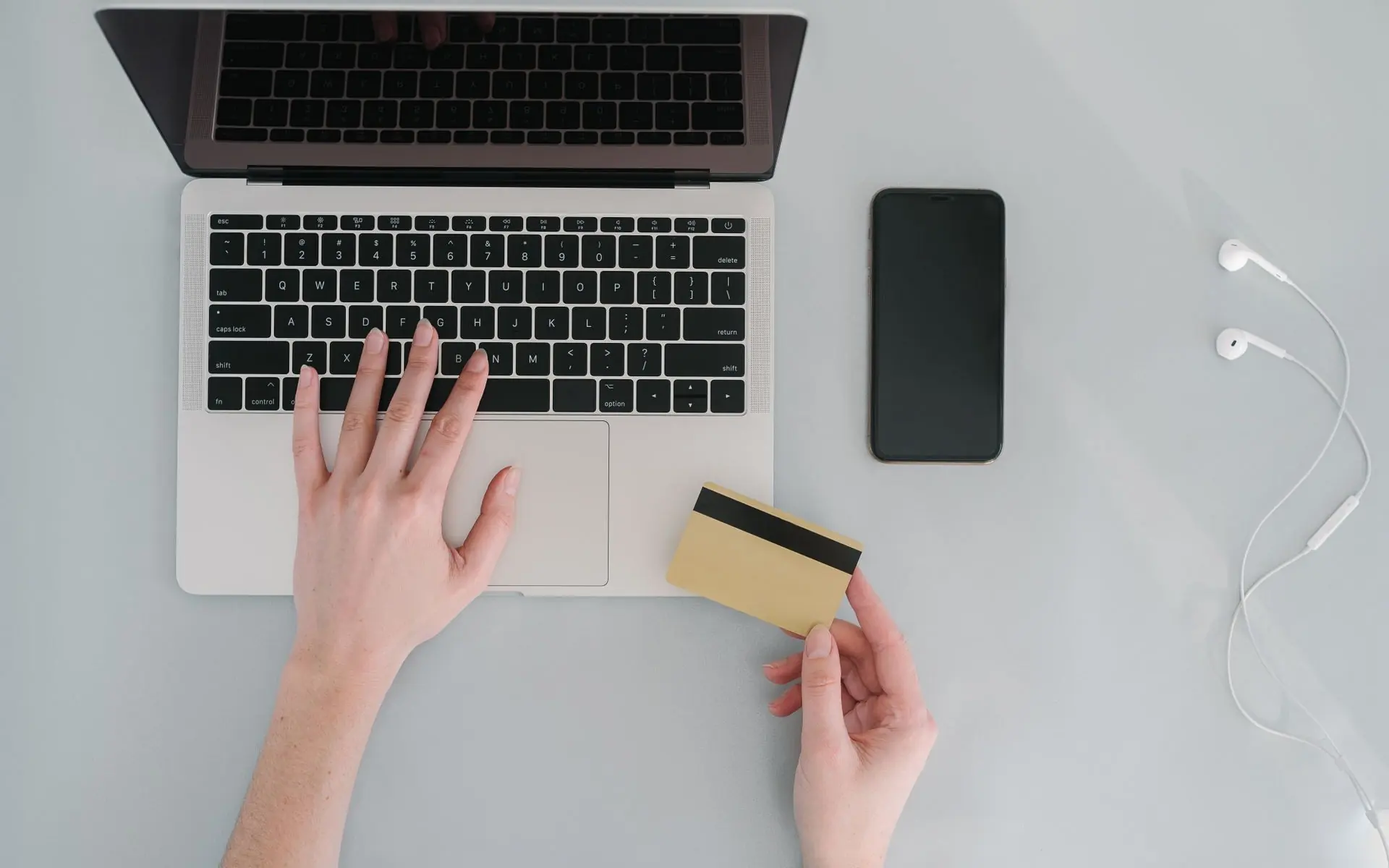 Person holding a bank card at a laptop during an online checkout.