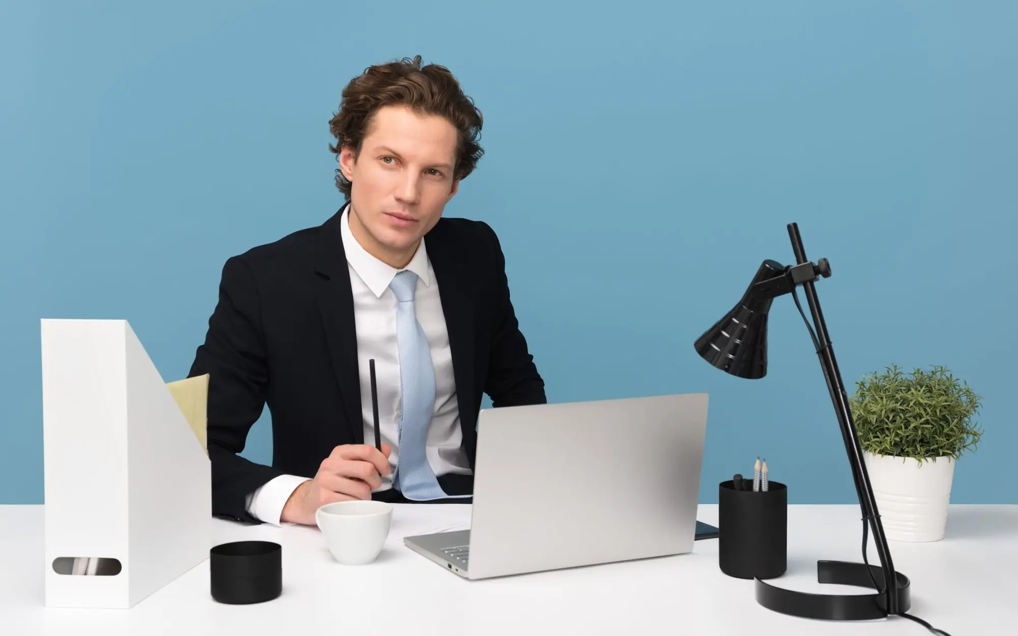 Man sitting with a laptop on a desk beside a lamp.