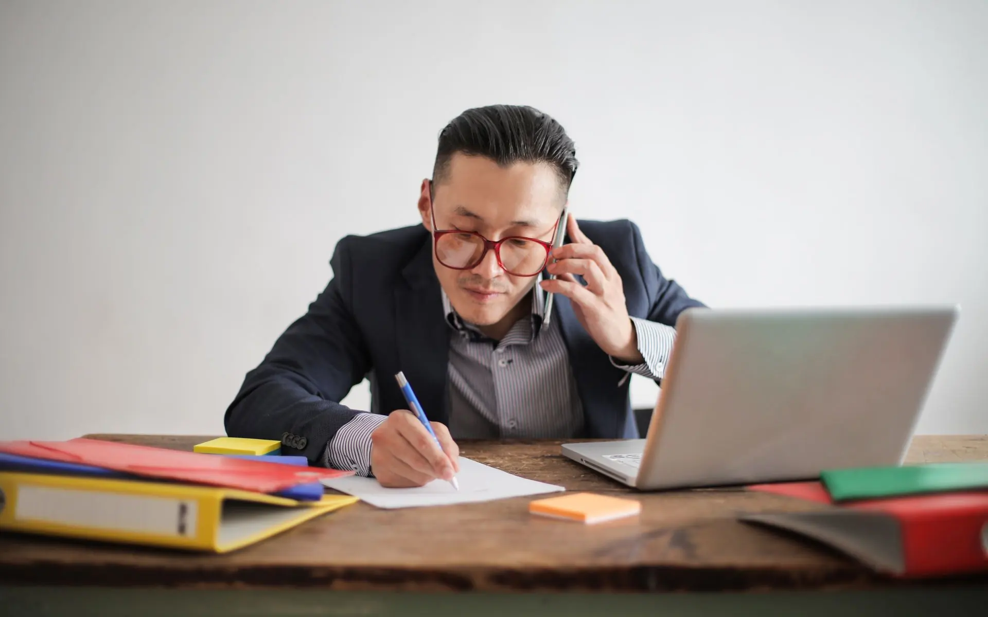 Man taking notes during a phone call at his laptop.