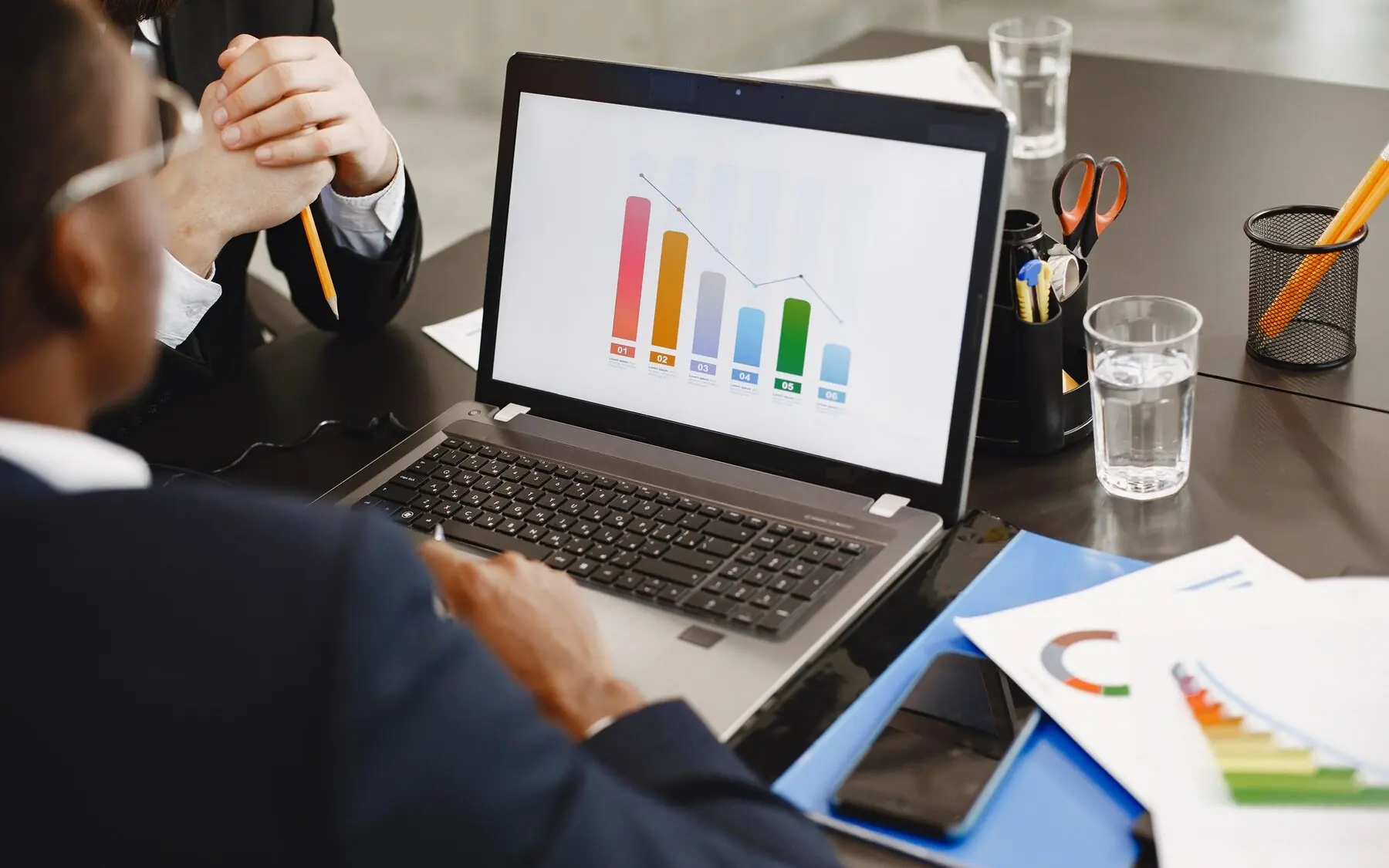 Two people reviewing bar graphs on a laptop in an office.