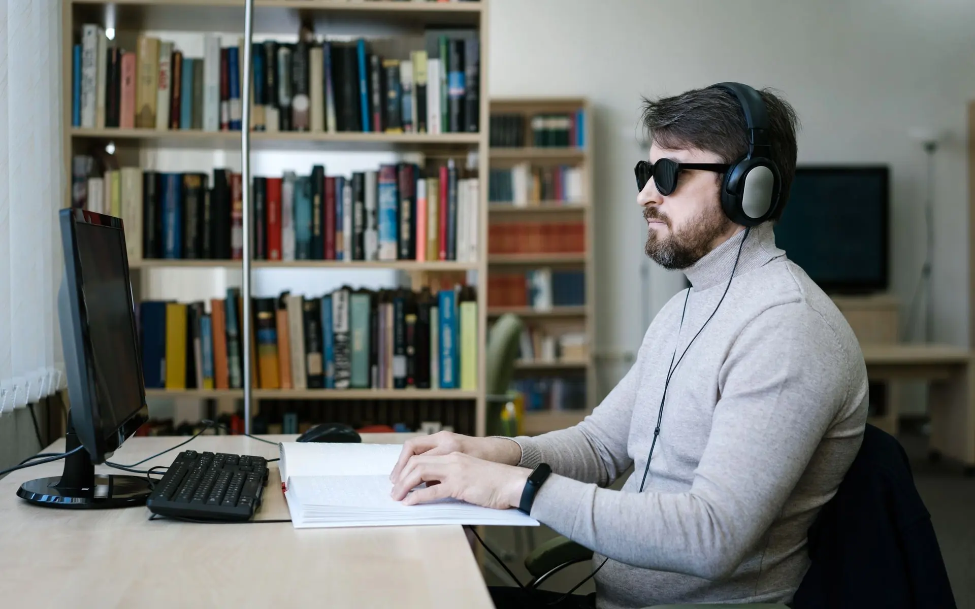 Man using a braille display and headset at a computer.