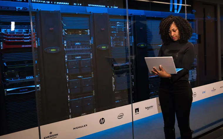 Engineer standing beside server racks with a laptop.