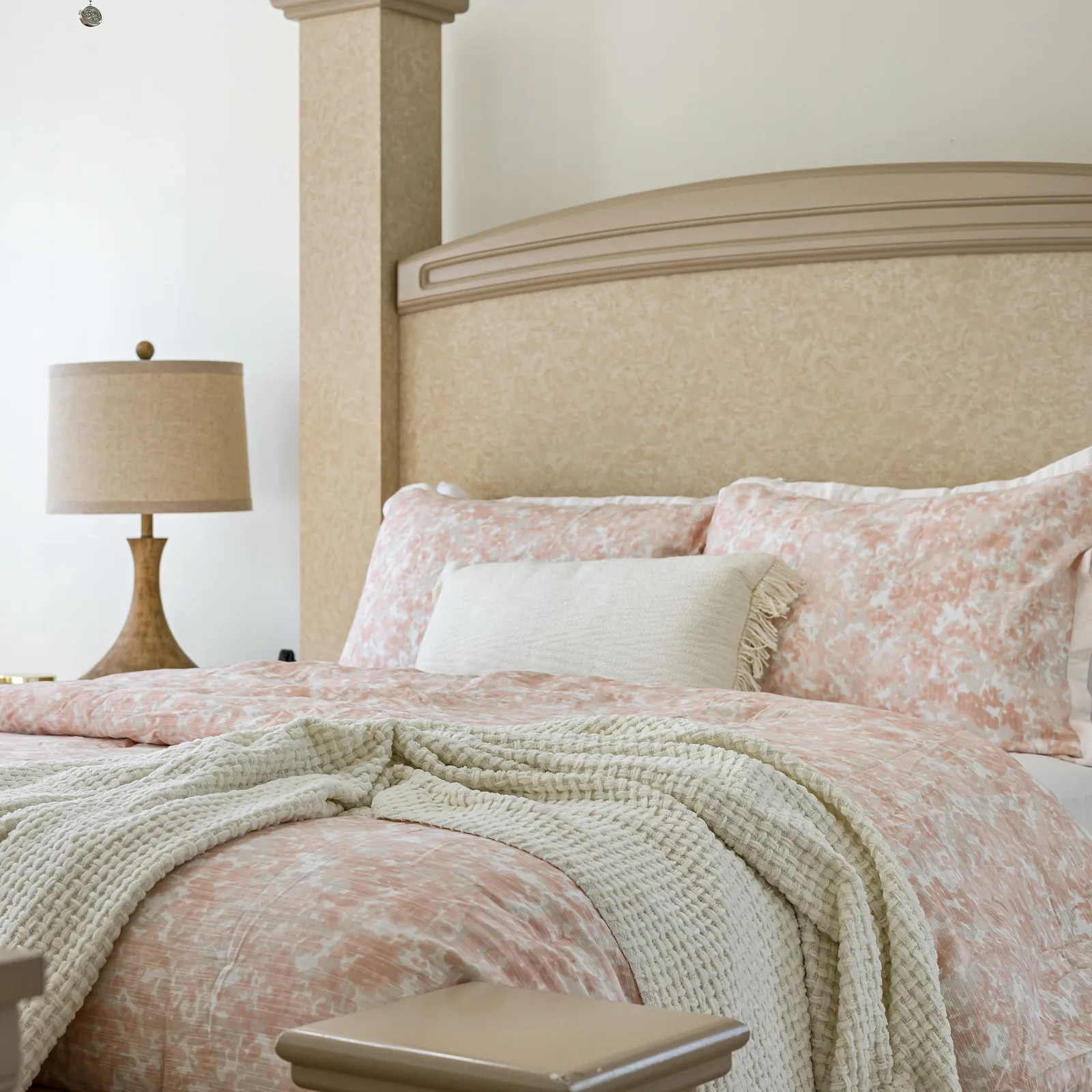 Bed made with a floral quilt cover, a waffle throw and a bedside lamp.