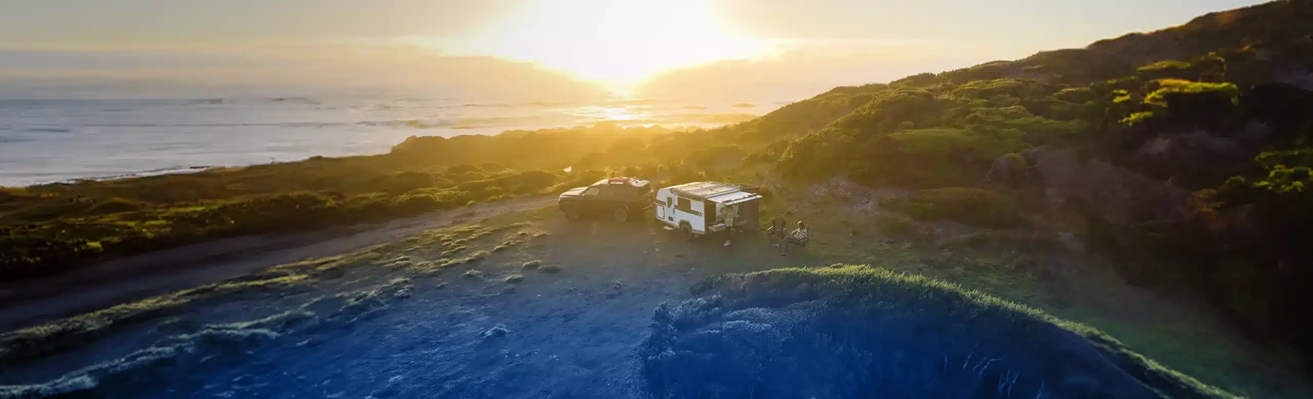 Caravan driving along a road at sunset.