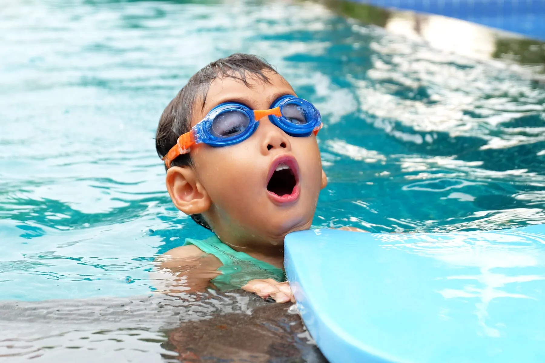Young boy in goggles during a swimming lesson, holding a kickboard.