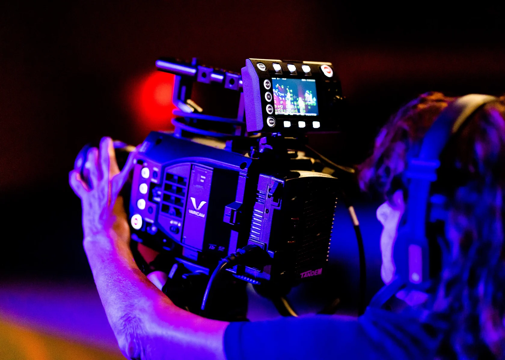 Camera operator working with professional cinema equipment under coloured studio lighting.