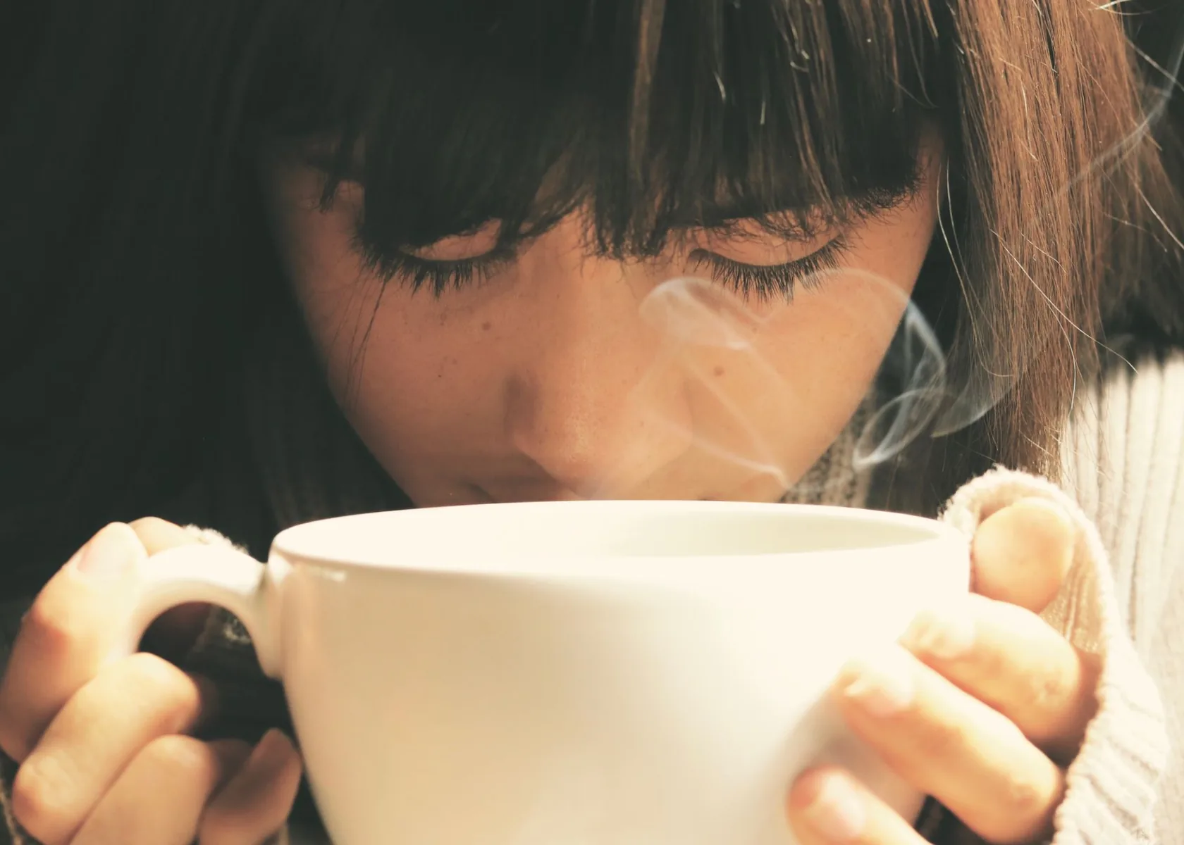 Woman warming her hands on a large cup of tea with steam rising.