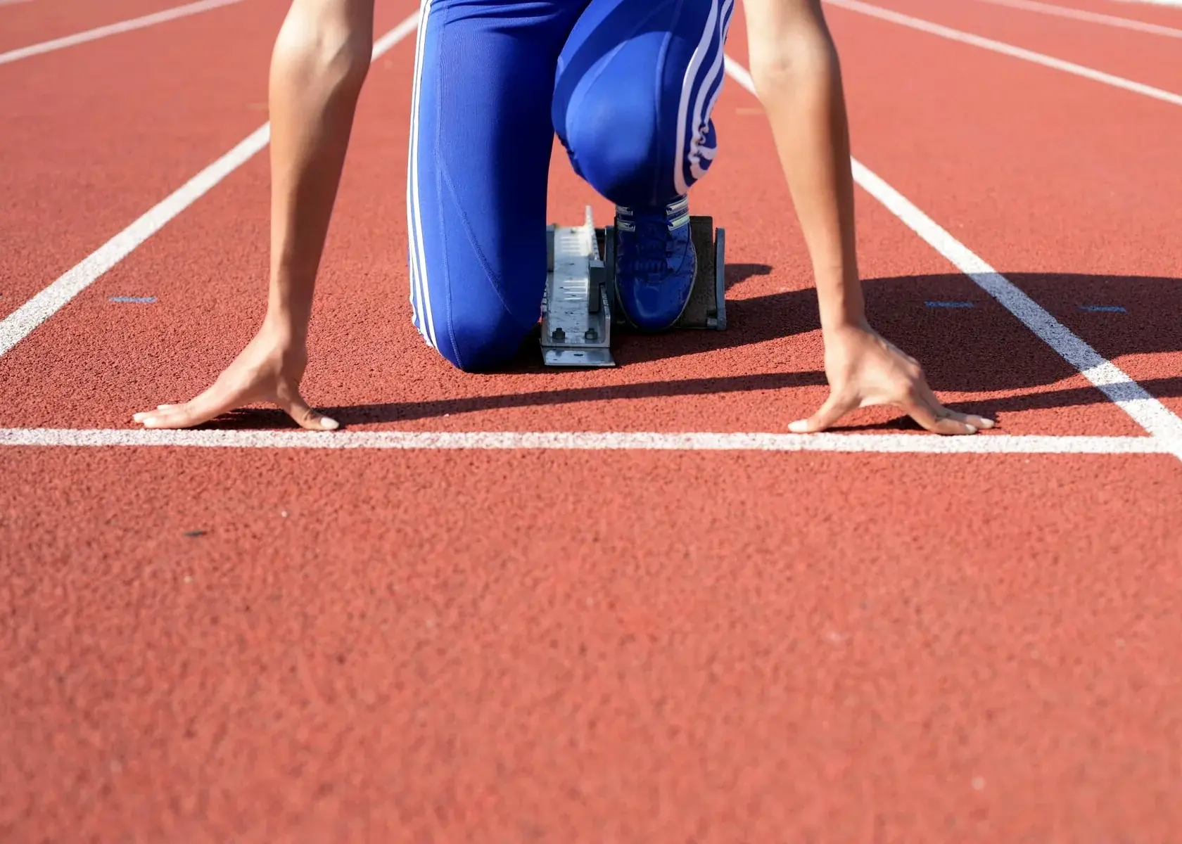 Athlete crouched in starting blocks on a red athletics track.