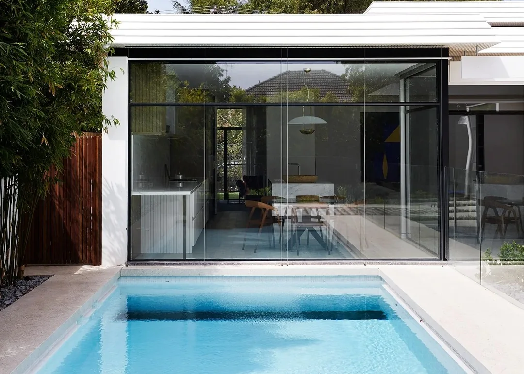 Glass pavilion with steel framed windows beside a swimming pool.