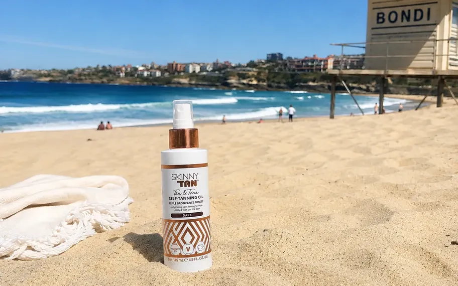Skinny Tan tanning oil bottle on Bondi Beach.