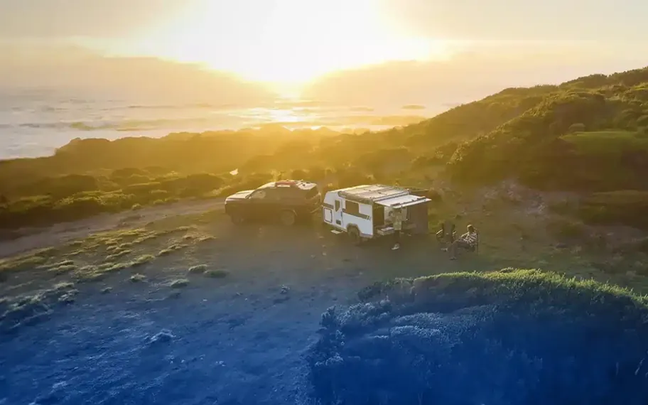 Caravan driving along a road at sunset.