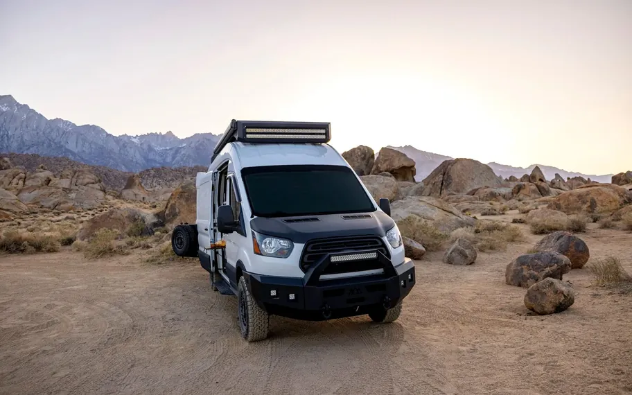 Off-road camper parked in a rocky desert landscape at dusk.