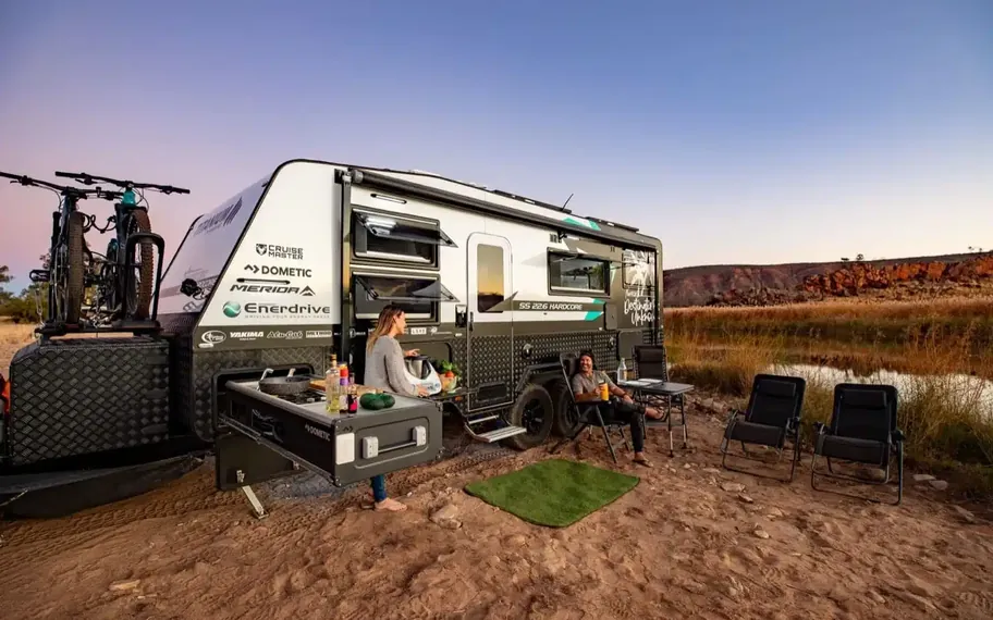 Caravan parked at a campsite with people outside.
