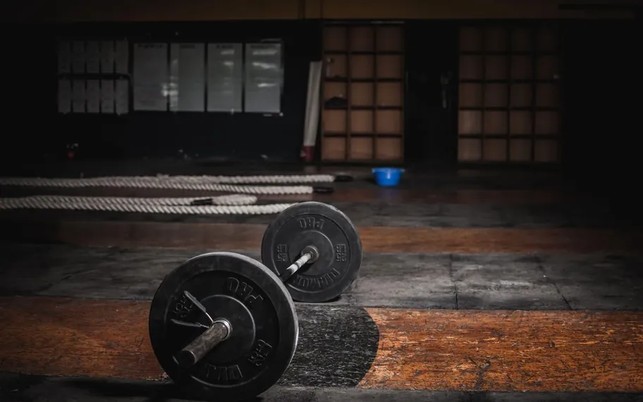 Barbell resting on a timber gym floor in low editorial light.