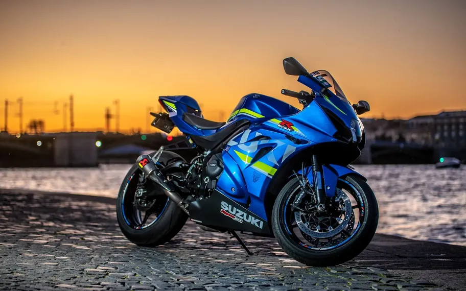Blue Suzuki GSX-R motorcycle parked on a cobbled waterfront at sunset.