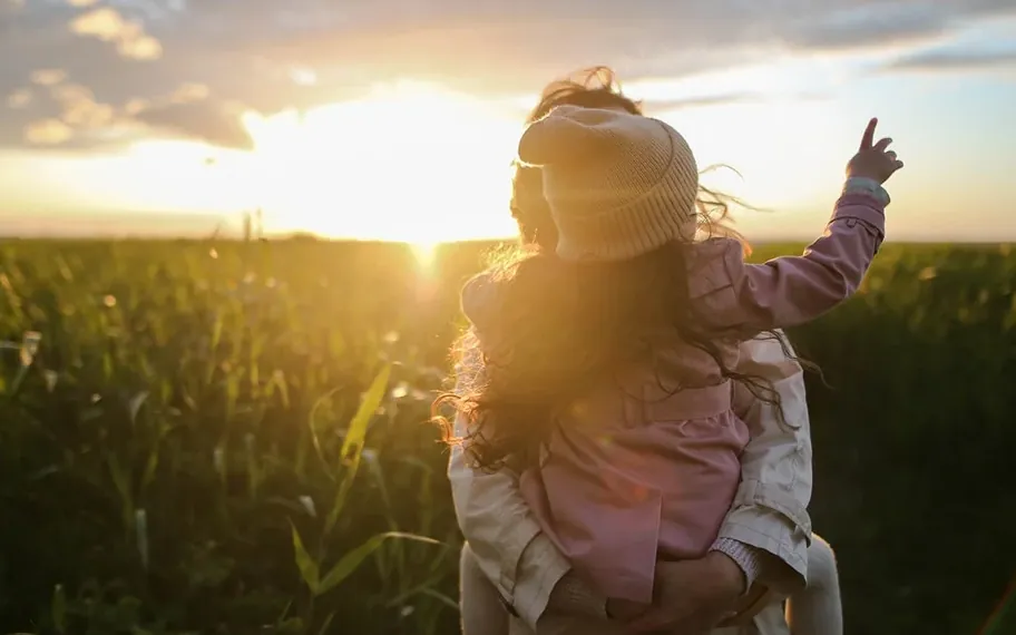 Adult carrying a child through a grassy field.