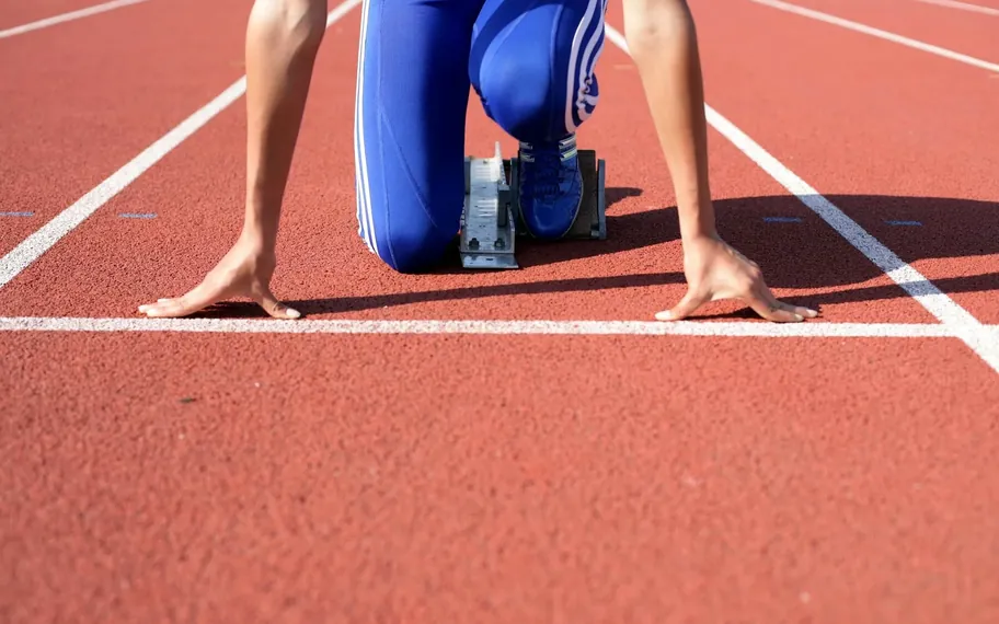Athlete crouched in starting blocks on a red athletics track.