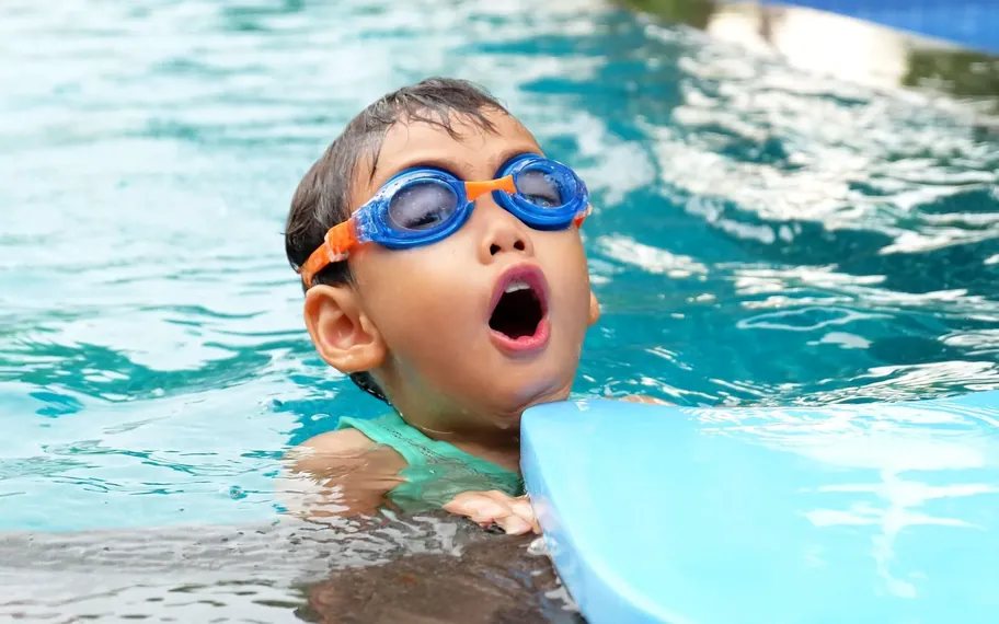 Young boy in goggles during a swimming lesson, holding a kickboard.